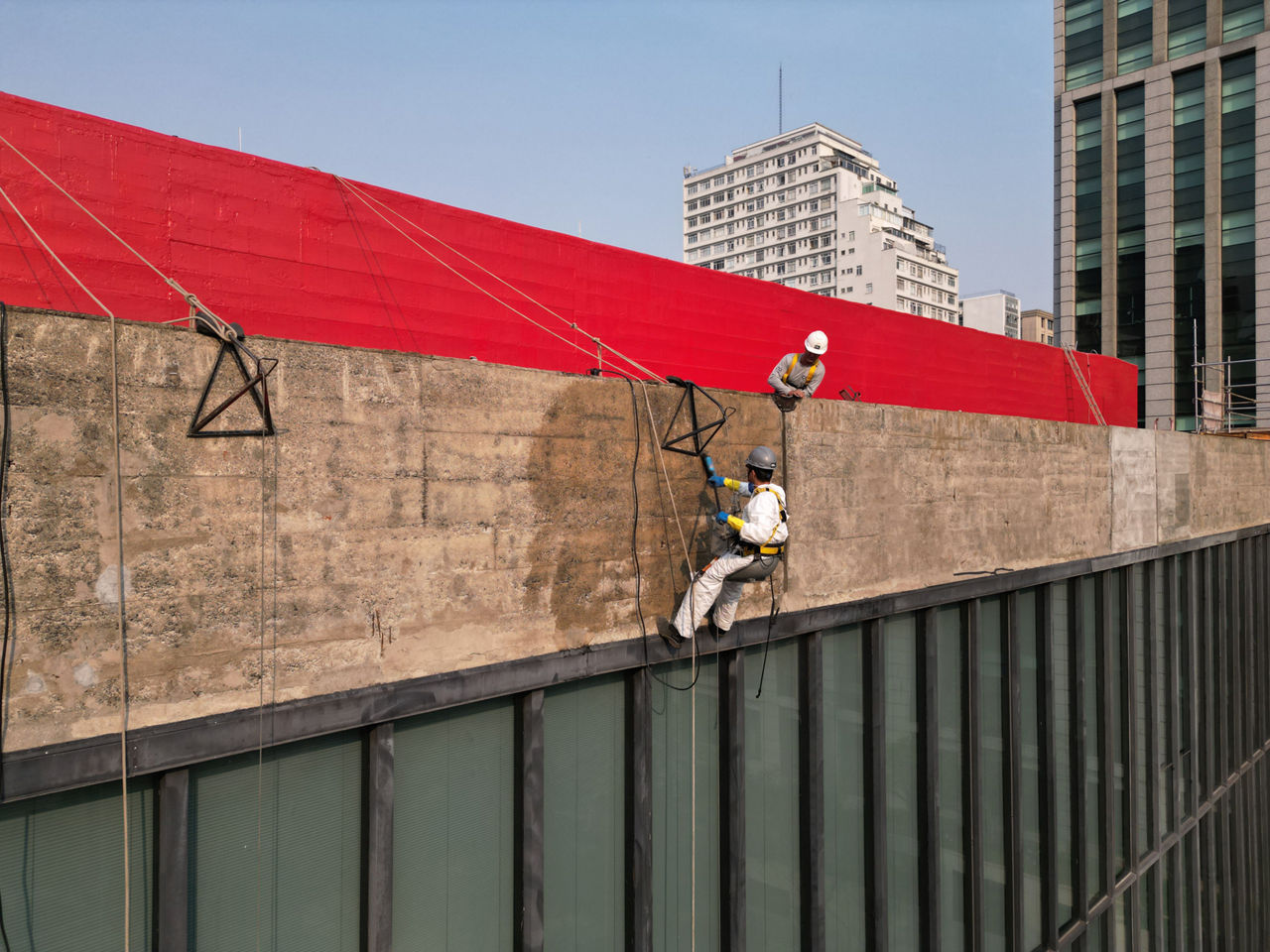 A worker hangs secured in front of the upper edge of the facade and sprays on Protectosil.