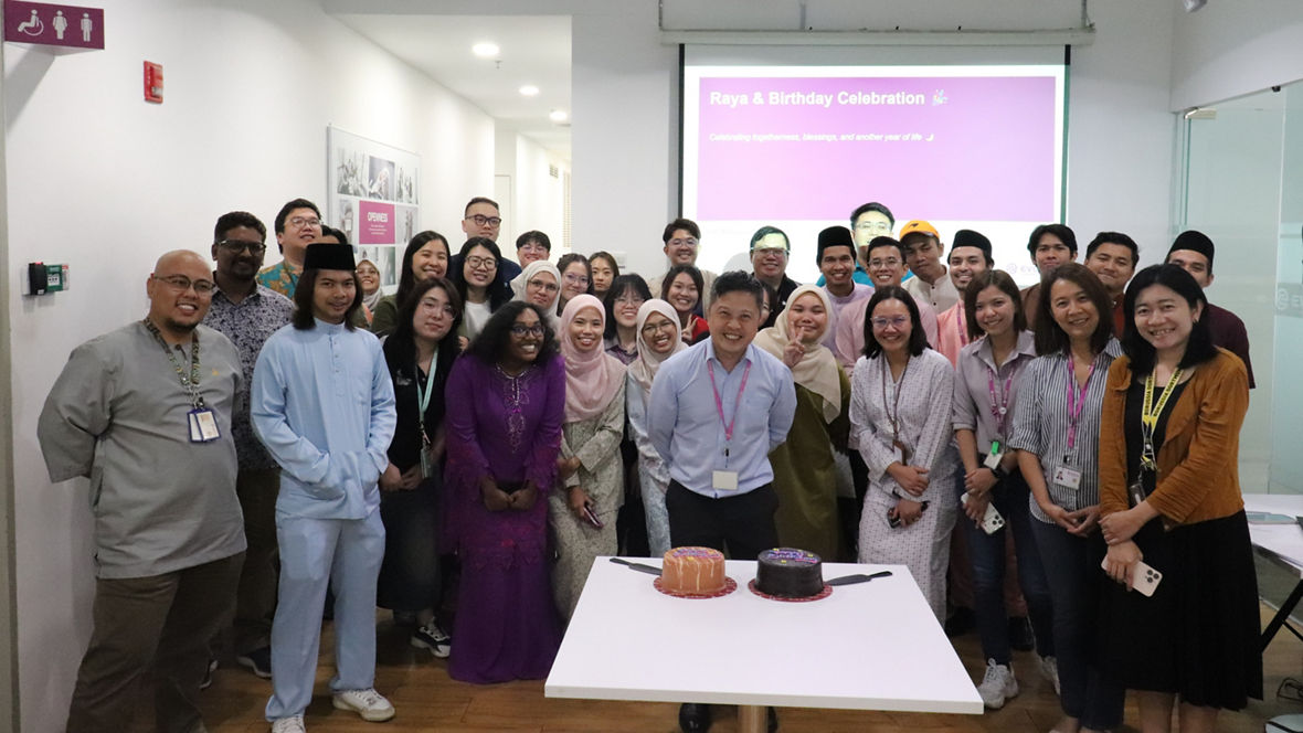 Group of people celebrating Raya and a birthday with cakes in an office setting.