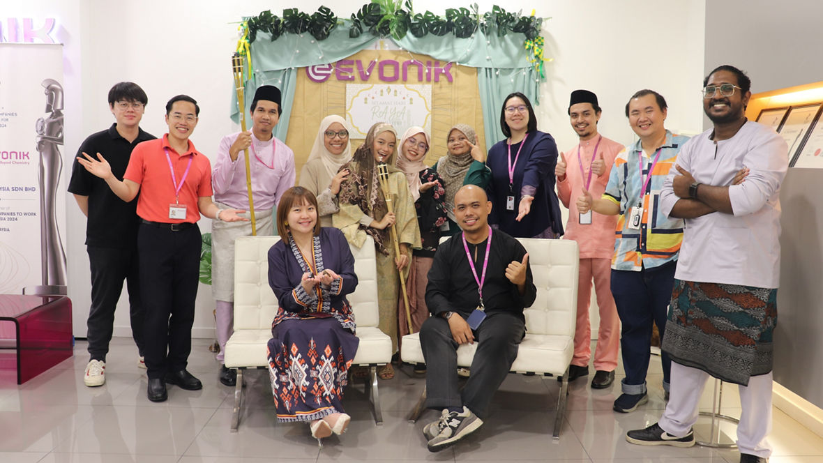 Group of people dressed in traditional attire posing in front of a festive backdrop with the Evonik logo.
