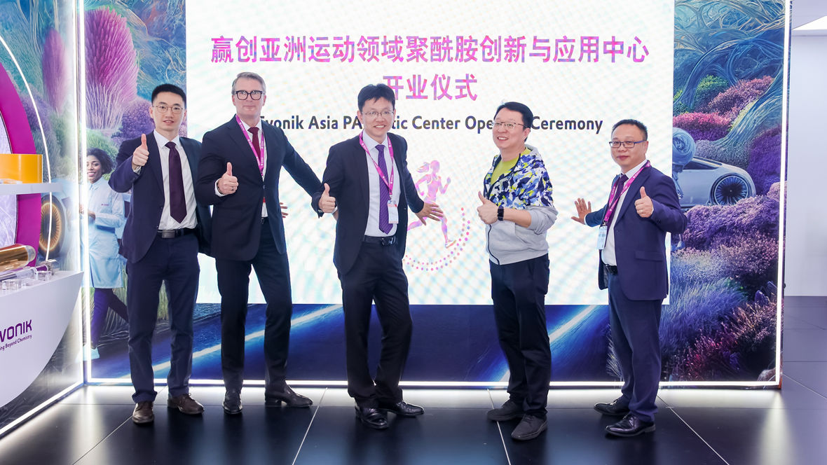 Five men in business attire posing with thumbs up at a corporate event with a colorful backdrop.