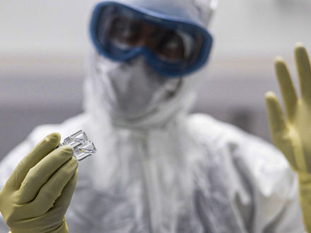 Ein Mann im Vollschutz mit Ganzkörperanzug, Schutzbrille und Gummihandschuhen hält zwei kleine Glasröhrchen.