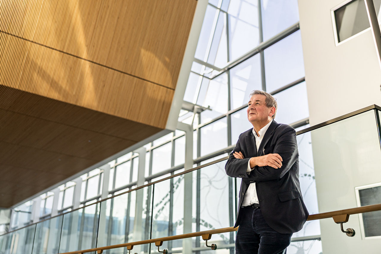 Dermot Kelleher steht mit verschränkten ARmen in einer großenn Halle mit Glasfront.