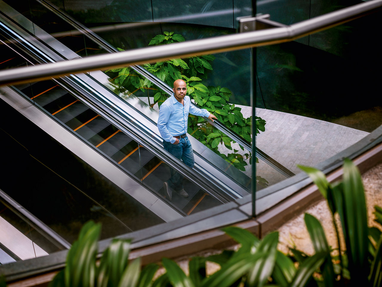 Gourab Mukherjee fährt auf einer Rolltreppe herab und schaut in die Kamera. 