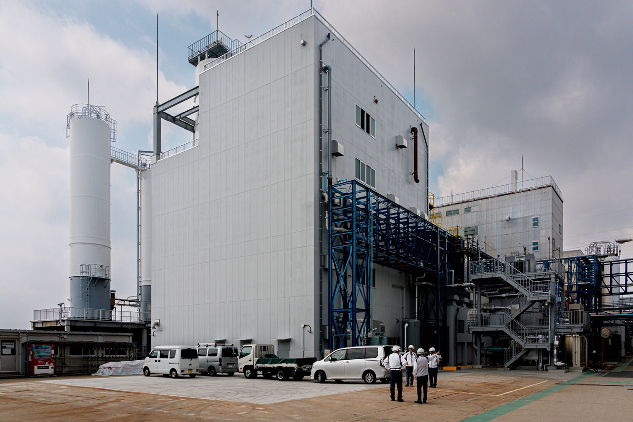 Ein großes, weißes Industriegebäude ohne Fenster mit zahlreichen Rohrleitungen.