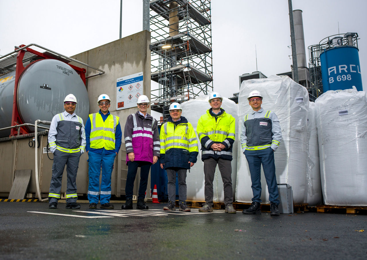 Six employees are standing in front of a chemical plant.