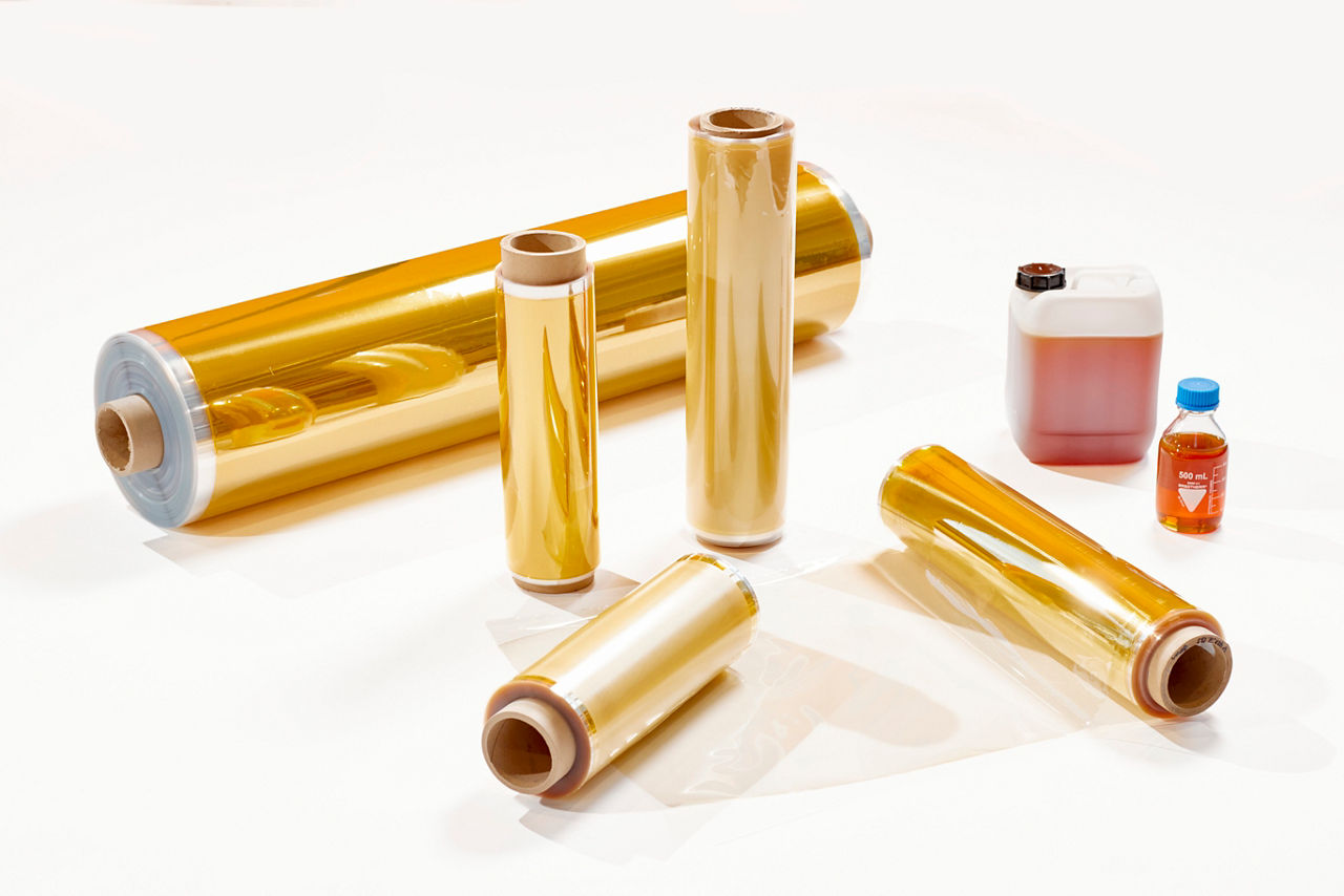 Several rolls of thin golden membrane film on spools and cut sections placed on a white surface, representing advanced ion exchange membrane materials used in electrochemical applications