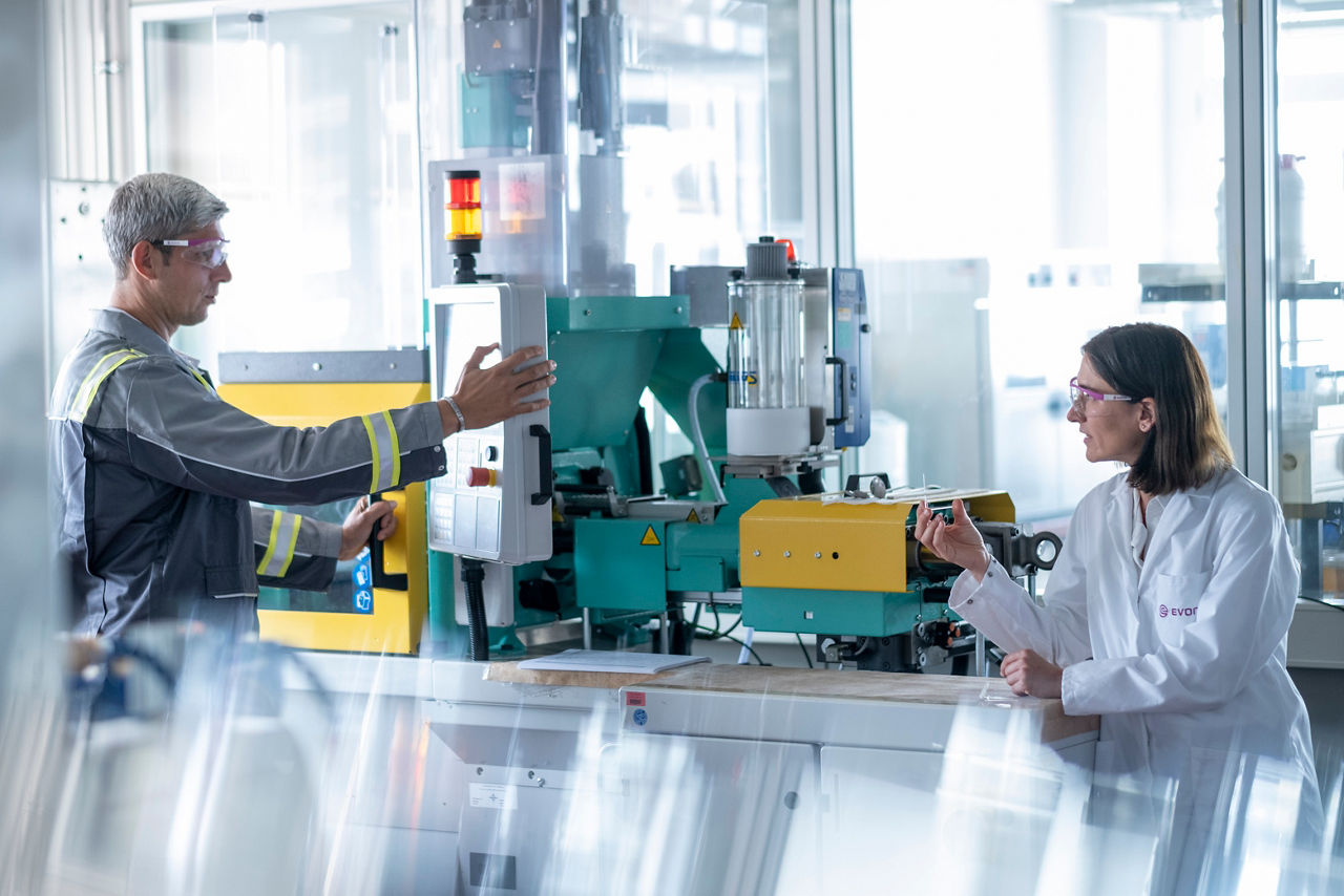 In this image, two professionals collaborate in a modern manufacturing facility, discussing machinery operations. This interaction emphasizes teamwork and communication, showcasing the importance of collaboration in enhancing process technologies within the chemical manufacturing sector at Evonik.
