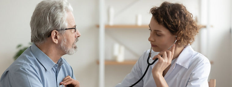 Focused young female cardiologist or general practitioner in white coat listening heartbeat or elderly senior male patient at checkup meeting, preventing cardiovascular disease, healthcare concept.