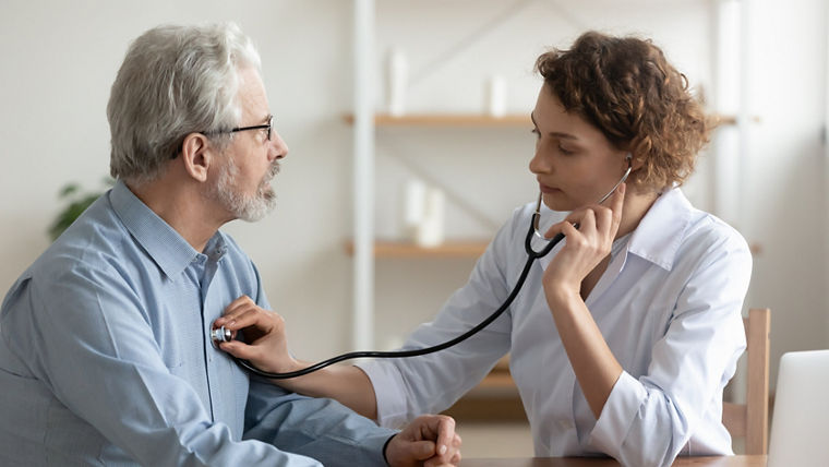 Focused young female cardiologist or general practitioner in white coat listening heartbeat or elderly senior male patient at checkup meeting, preventing cardiovascular disease, healthcare concept.