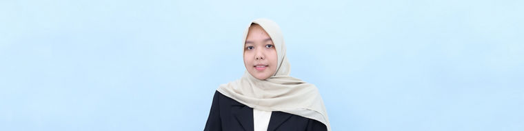 Young woman wearing a beige hijab and black blazer sitting against a light blue background.