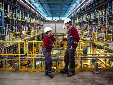 Eine Mitarbeiterin und ein Mitarbeiter stehen in der Fermenterhalle der Rhamnolipidproduktion in Slovenská Ľupča, Slowakei, und unterhalten sich.