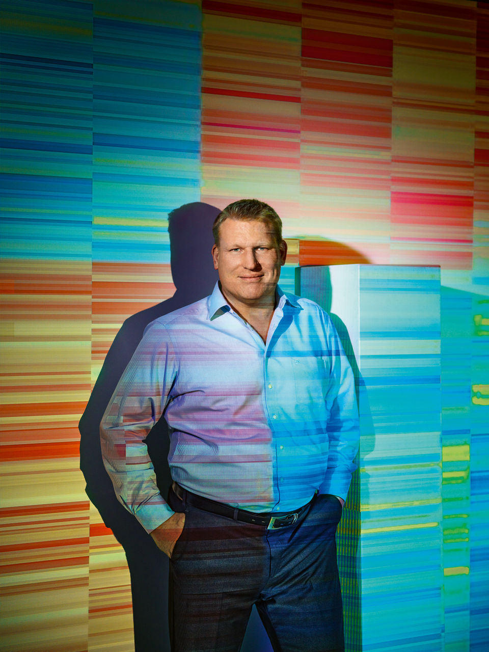 Florian Böhl is standing in front of a wall. Colored methylation patterns are projected onto him and the wall.