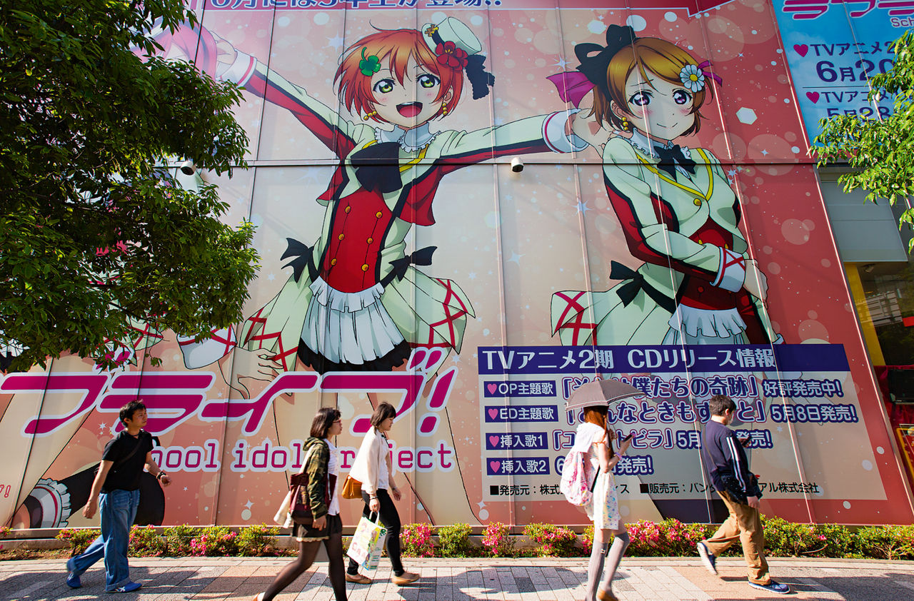 Five people walk past large manga drawings on the wall of a house.