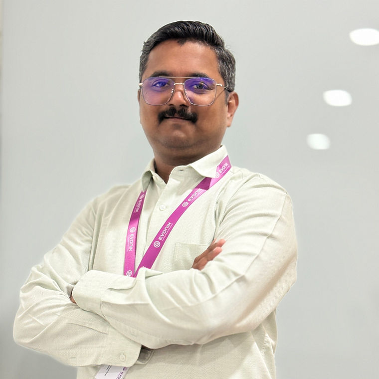 Man wearing a light-colored shirt and a purple lanyard, standing with arms crossed.