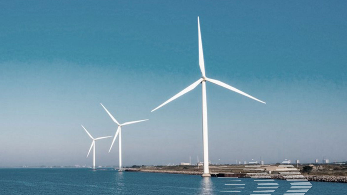 Three large white wind turbines stand along a coastline under a clear blue sky.