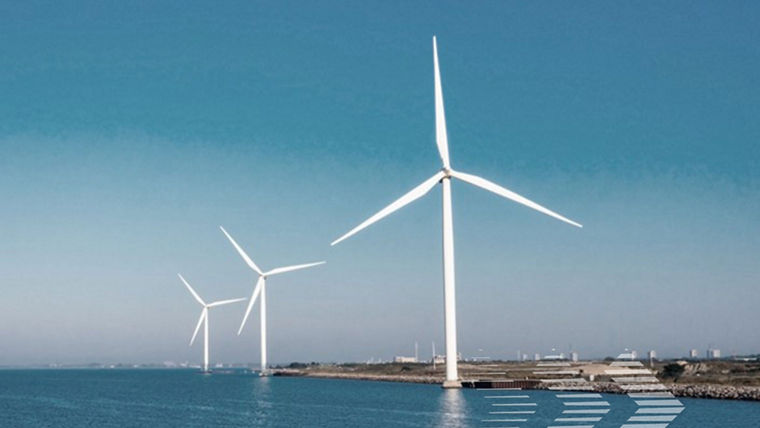 Three large white wind turbines stand along a coastline under a clear blue sky.