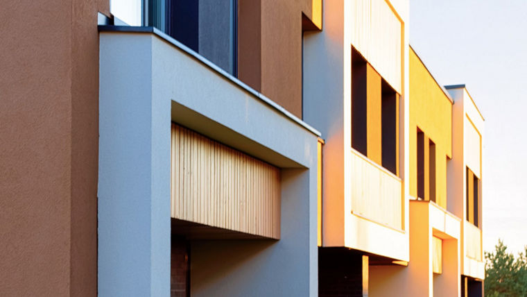 Modern residential building facade with vertical wooden panels and small evergreen trees in front.
