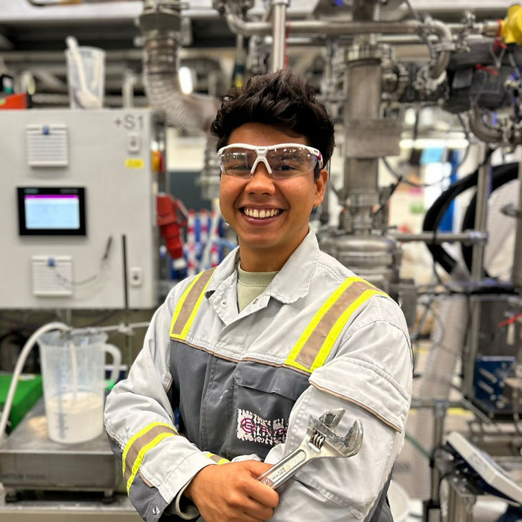 Person in a reflective safety jacket holding a large adjustable wrench in an industrial setting.