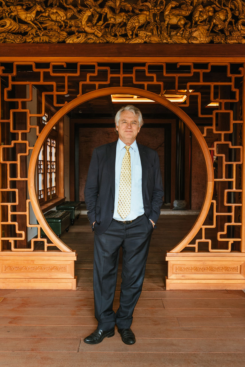 Jörg Wuttke in a suit in front of an almost circular wooden arch with modern ornaments.