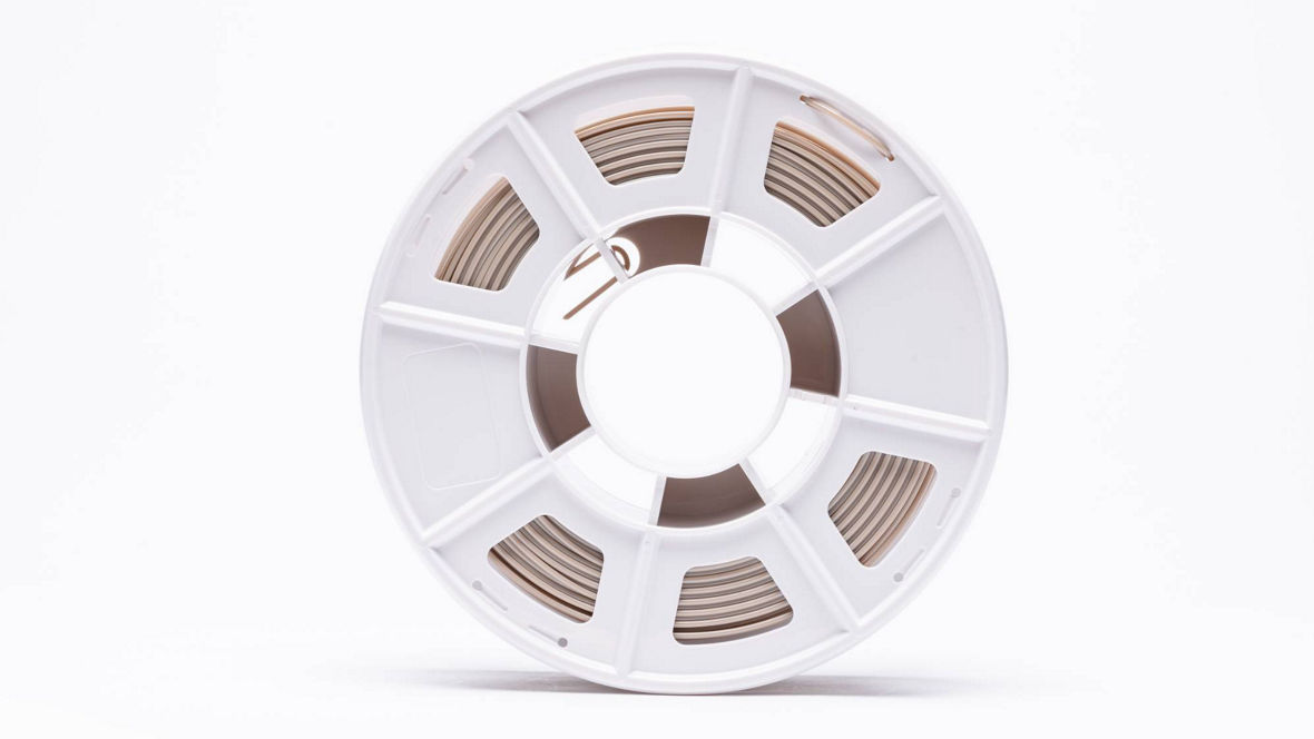 A close-up view of a spool of INFINAM® PEEK filament for industrial applications, showcasing its white plastic design and the neatly arranged filament strands inside.