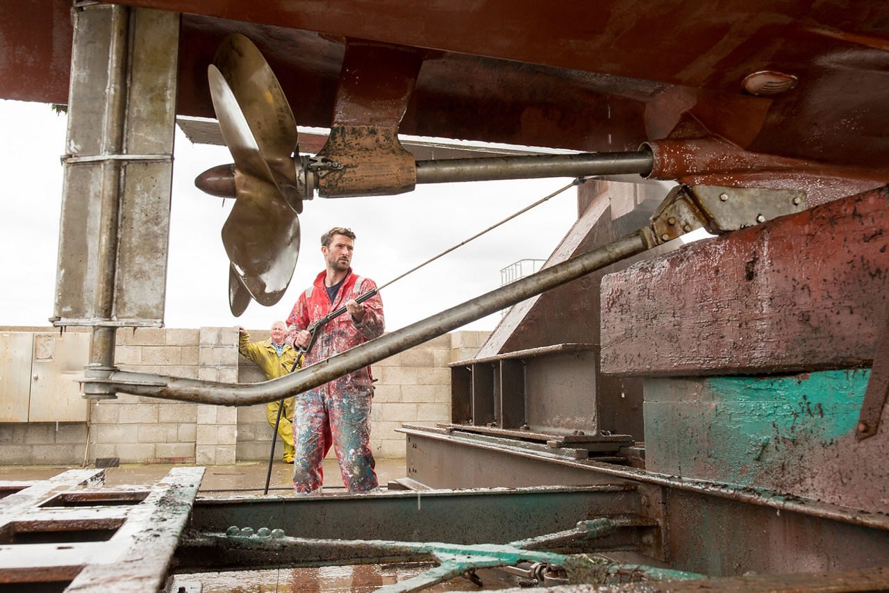 A ship painter cleaning the hull and propeller with a high-pressure washer