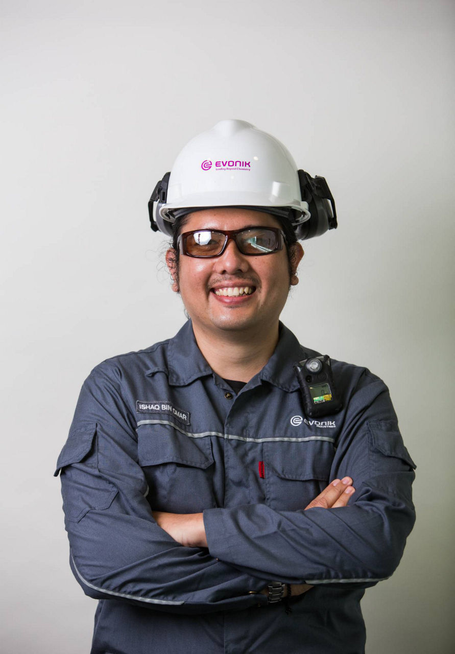 A worker in a safety helmet and uniform with Evonik branding, standing confidently with arms crossed.