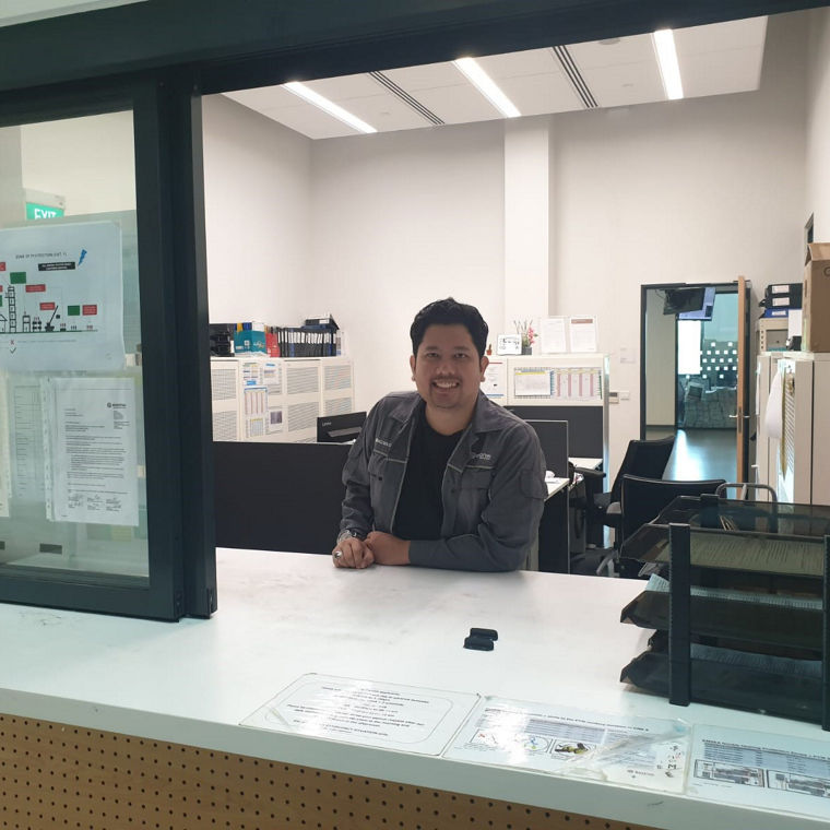 A reception area with a staff member at a service counter and office space in the background.