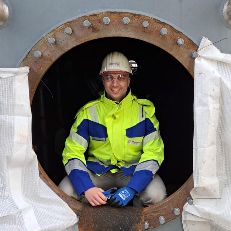 A worker in a high-visibility jacket and gloves sits in an industrial opening, ready for maintenance tasks.