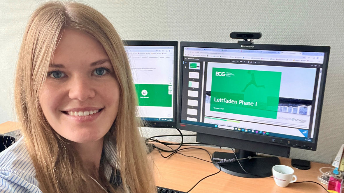 A person at a desk with two monitors displaying a presentation titled "LeitLaden Phase I" and a cup on the table.