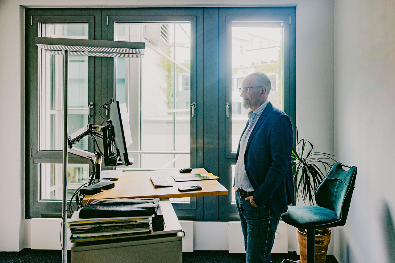 Johann Meierhöfer steht in seinem Büro an einem hochgefahrenem Schreibtisch.