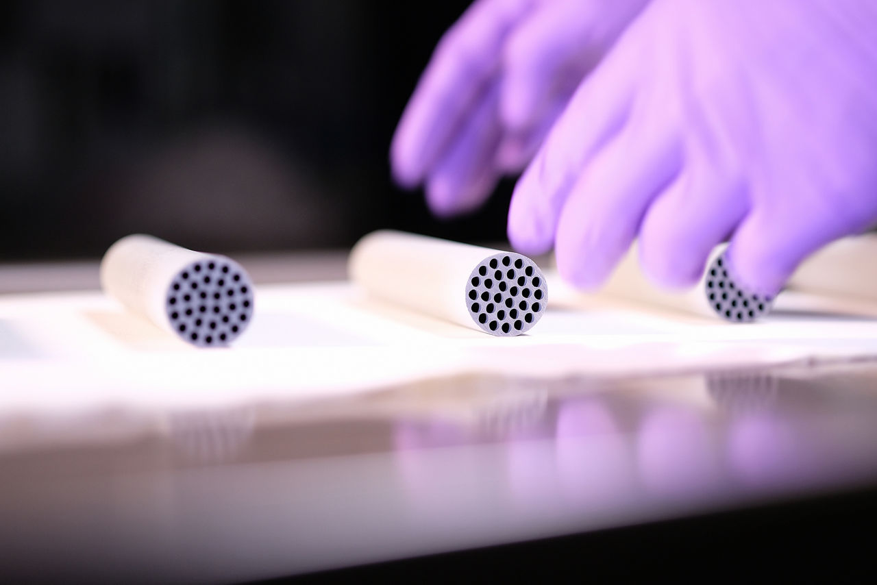 Zwei Hände in Handschuhen greifennach einem zylinderförmigen Katalysator.