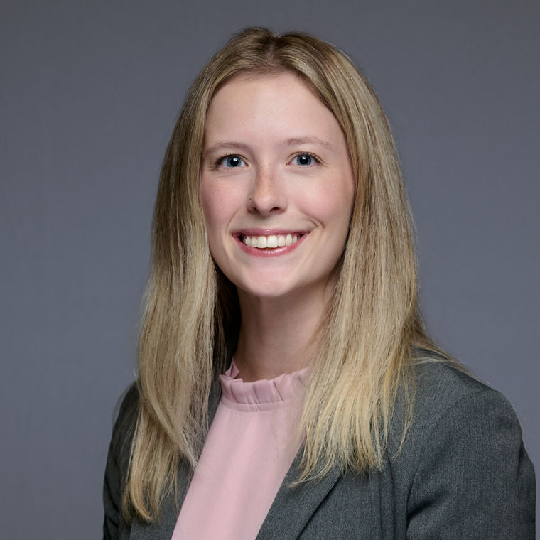 Professional portrait of a person with long blonde hair wearing a gray blazer and pink blouse.