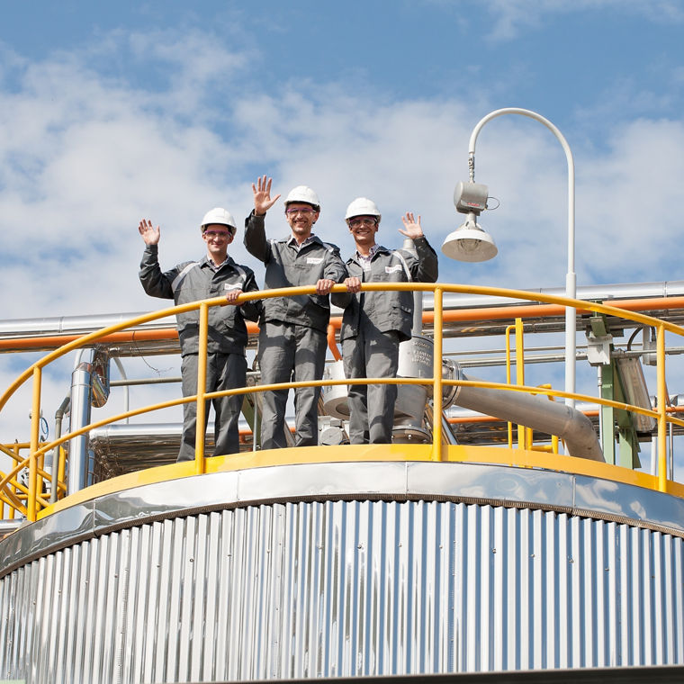 Vier Mitarbeiter stehen auf einem lagerbehälter un winken.