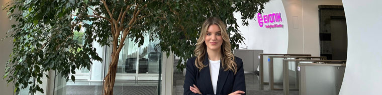 Person standing with arms crossed in a modern office lobby with a large potted tree and Evonik logo in the background.