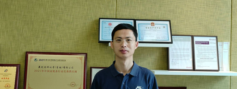 A person stands in front of a wall displaying various awards and certificates.