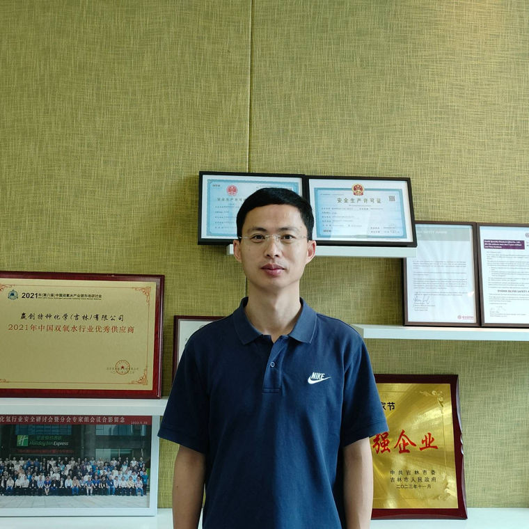 A person stands in front of a wall displaying various awards and certificates.