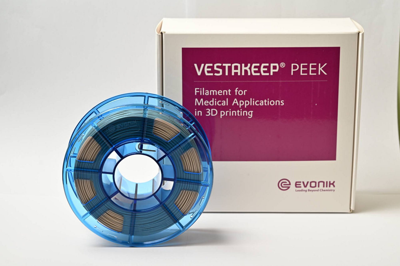 Close-up view of a blue spool of VESTAKEEP® PEEK filament, prominently displayed next to its packaging. The spool features a series of brown filaments wound neatly, indicating its use for medical applications in 3D printing. The packaging clearly labels the product as suitable for healthcare innovations, emphasizing its biocompatibility and durability, making it ideal for professionals in the medical field.