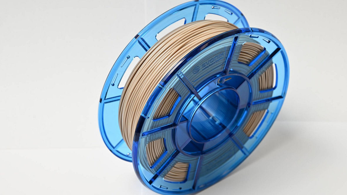 The image features a spool of 3D printing filament, showcasing a smooth, beige-colored filament neatly wound around a transparent blue spool. The spool has a circular shape with a central hub that allows it to rotate freely. The blue plastic is semi-transparent, revealing the filament inside, while the cutouts in the spool design provide a modern aesthetic and allow visibility of the filament's quantity. The background is minimalistic, emphasizing the spool's professional appearance, making it suitable for both hobbyists and professionals in the 3D printing field. The overall look conveys a sense of quality and precision, essential for creating detailed 3D models.