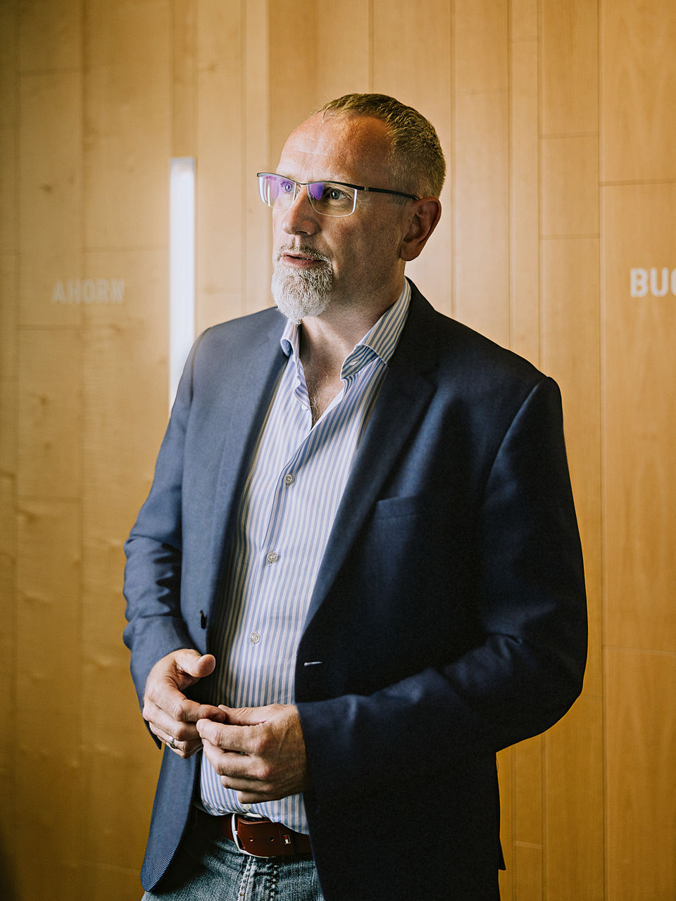 Johann Meierhöfer steht vor einer Wand aus verschiedenen Holzarten.