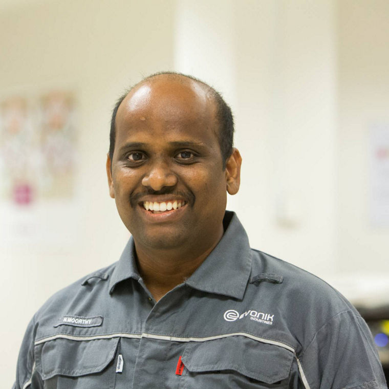 A worker wearing a gray uniform with the Evonik logo, standing in an office environment.