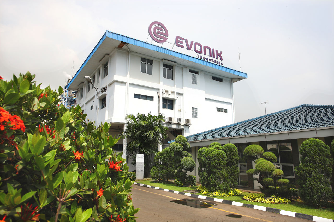 Evonik building with a blue roof and logo, surrounded by well-maintained greenery and flowers.