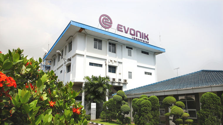 Evonik building with a blue roof and logo, surrounded by well-maintained greenery and flowers.
