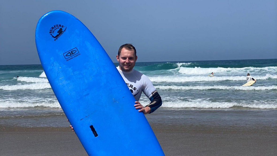 A person holding a blue surfboard on the beach with waves in the background.