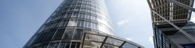 Glass-covered modern skyscraper viewed from below with a curved metal canopy structure overhead - the Evonik Tower.