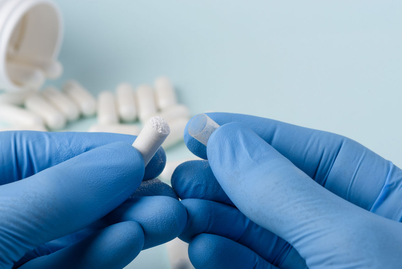 Medicine pill open in doctor hands with white powder inside and bottle on background
