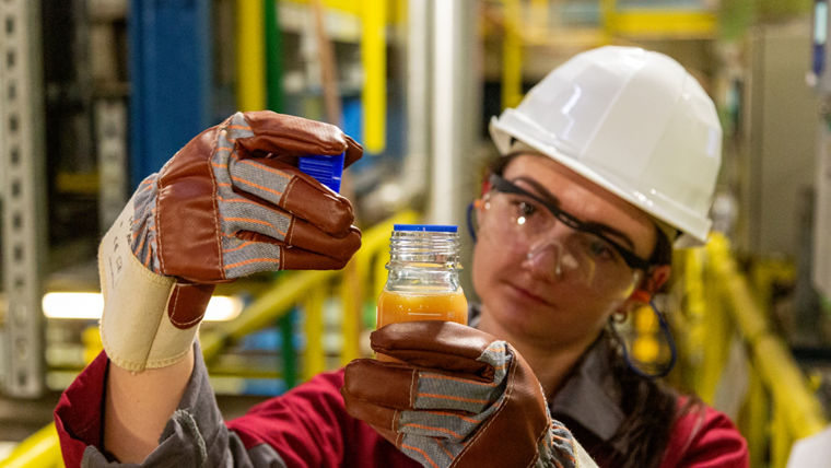 EIne Ingeneurin verschraubt eine Probe aus einer kleinen Glasflasche mit einer orangfarbenen Flüssigkeit.