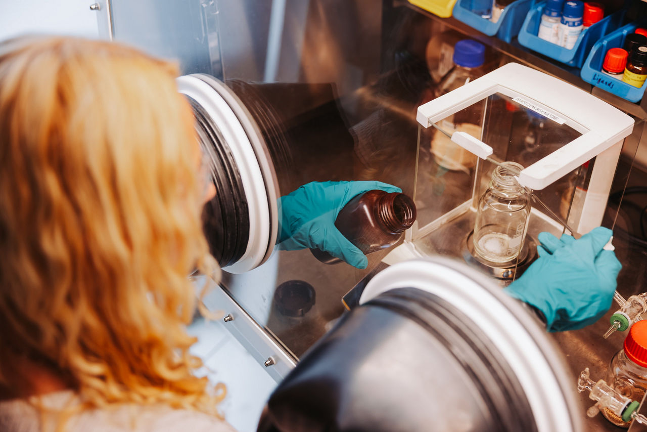 Lisa Steinwachs fills a measuring cylinder with white powder under protective conditions.