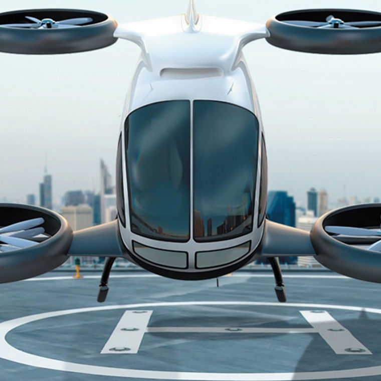 A futuristic white drone with four large rotors hovering above a rooftop helipad in a city.