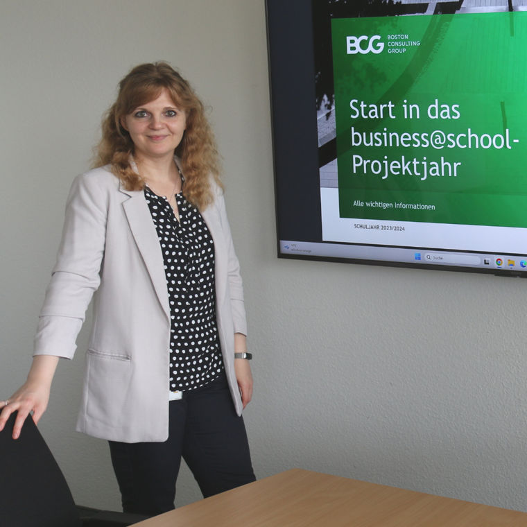 A woman stands beside a screen displaying a presentation about the business@school project year by BCG.