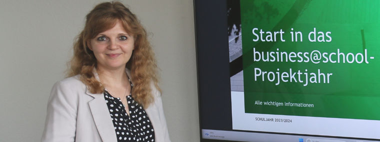 A woman stands beside a screen displaying a presentation about the business@school project year by BCG.